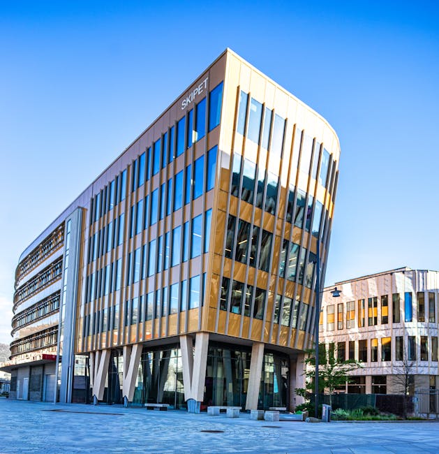 An exterior view of a modern office building with a curved façade featuring large reflective glass windows and vertical wooden panel accents, situated in Stockley Park. The building stands on a paved